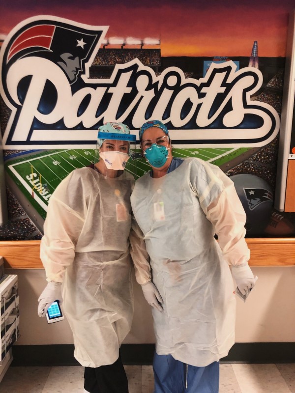 Cheryl and Caitlyn Dowd, gowned and masked, pose in front of a Patriots mural.