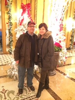 A happy couple stands in front of a glittering holiday display of lights and garlands.