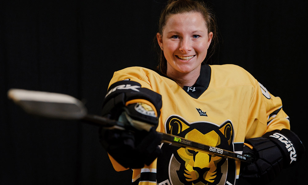 Meghan McManus holding a hockey stick in a Boston Pride jersey
