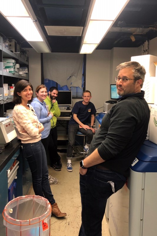 Five lab members posed casually in a small, cramped laboratory.