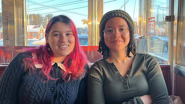 Two people sitting together in sunlit diner booth.