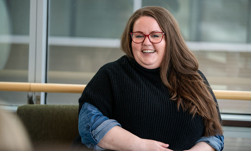 Kelley Jones sitting wearing red glasses, smiling.