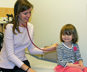 A toddler girl smiles as a doctor listens to her lungs with a stethoscope.