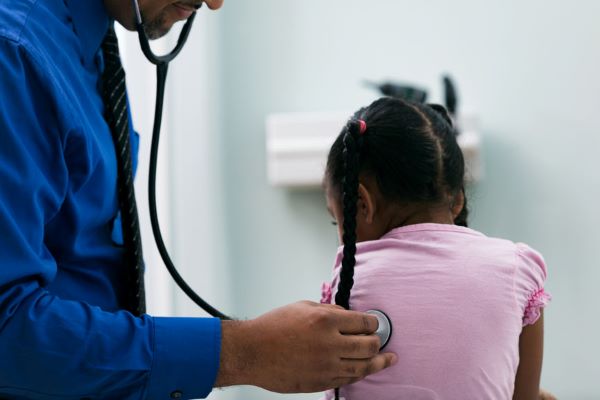 A doctor presses a stethoscope to a child's back