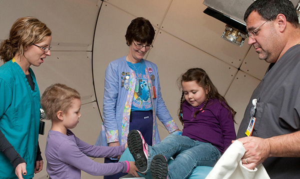 Mia makes Veronica comfortable before proton therapy, while Rachel Bolton, RN, (center) and other staff look on.