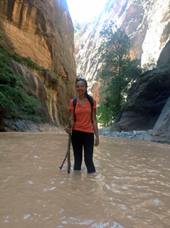 Aisha James calf-deep in the muddly water of a river running through a stony gorge
