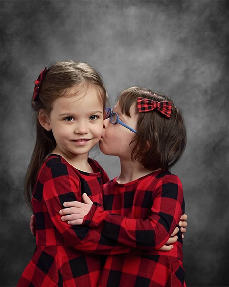Josie Murray kisses her twin sister, Maddie, on the cheek for a school picture.