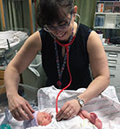 Dr. Randazzo-Ahern smiles as she leans over a newborn's crib and listens to its heart.
