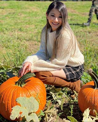 Olivia Shyong kneels in a pumpkin patch.