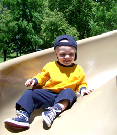 A grinning toddler comes down a slide.