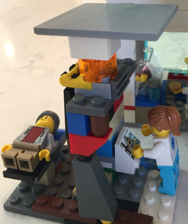 A Lego patient lies on a Lego treatment table while a Lego technician oversees the treatment in a tiny Lego treatment lab.