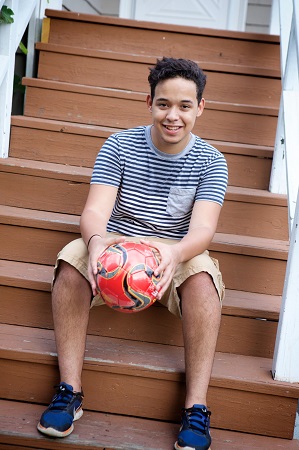 Josh Canales sits on his front porch holding a soccer ball. 