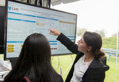 A researcher points to data on a screen as she explains her research to a listening woman.