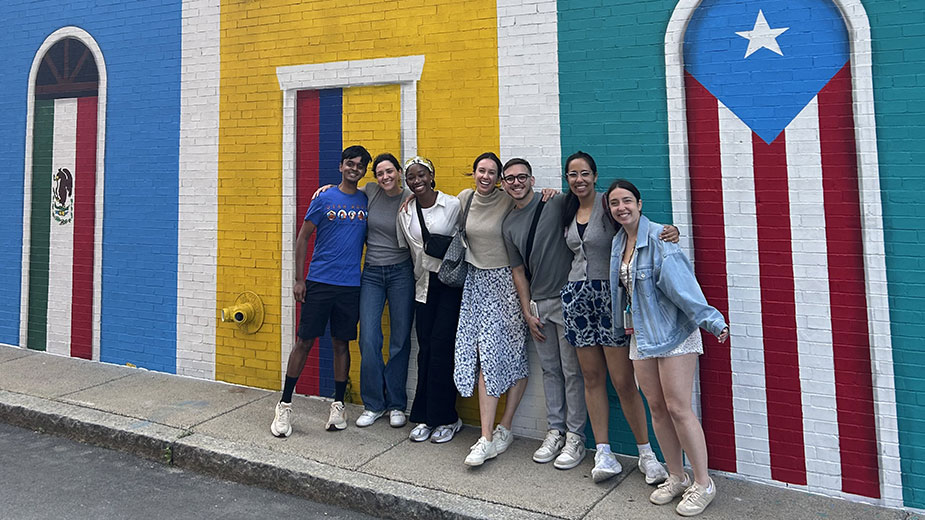 A group of people standing in front of a colorful street with flags on the doors