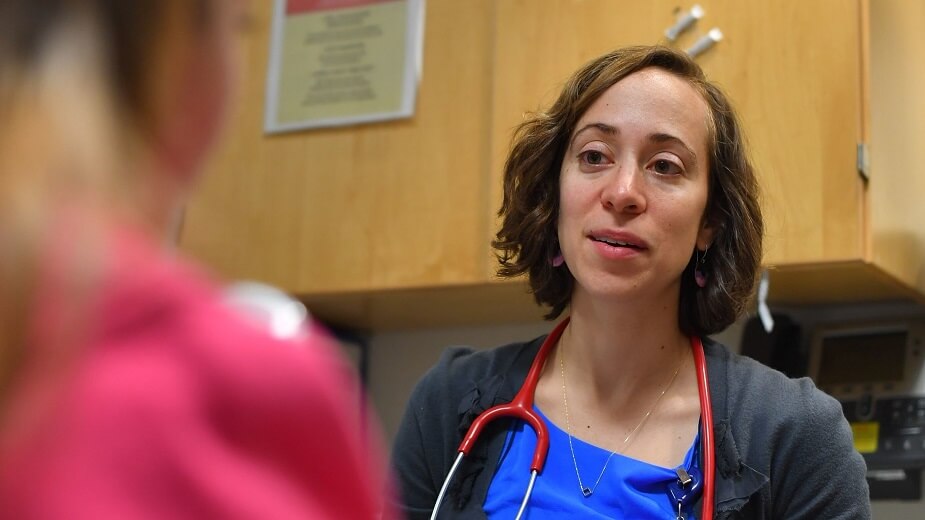 A doctor speaks to a female patient who is only partially seen by the camera