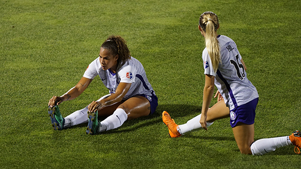 two woman sitting on a soccer field stretching