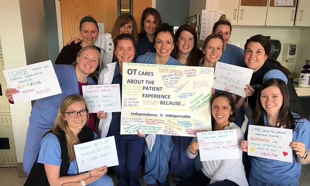 Occupational therapy nurses smile while holding patient experience signs.