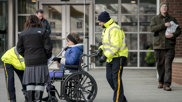 Two security officers help a patient in a wheelchair. Two security officers help a patient in a wheelchair.