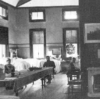 A long table and white-blanketed beds in Ward A, circa 1916.