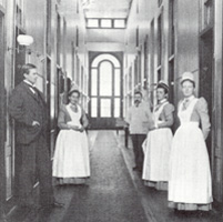 Aproned nurses and a doctor standing in the hallway of Ward E, circa 1912.