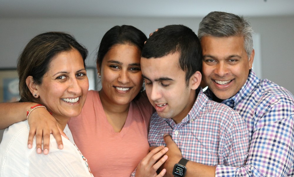An Indian family hugs their teenaged son.
