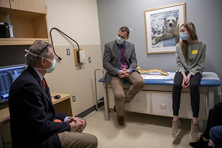 Meg Armstrong sits on an exam table while Dr. Braun and Dr. Grottkau do a consult.