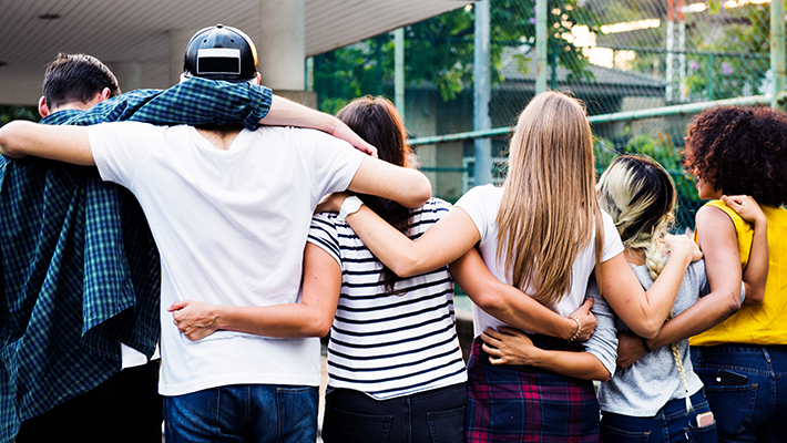 Photo of six teens with their backs to the camera and their arms around each other