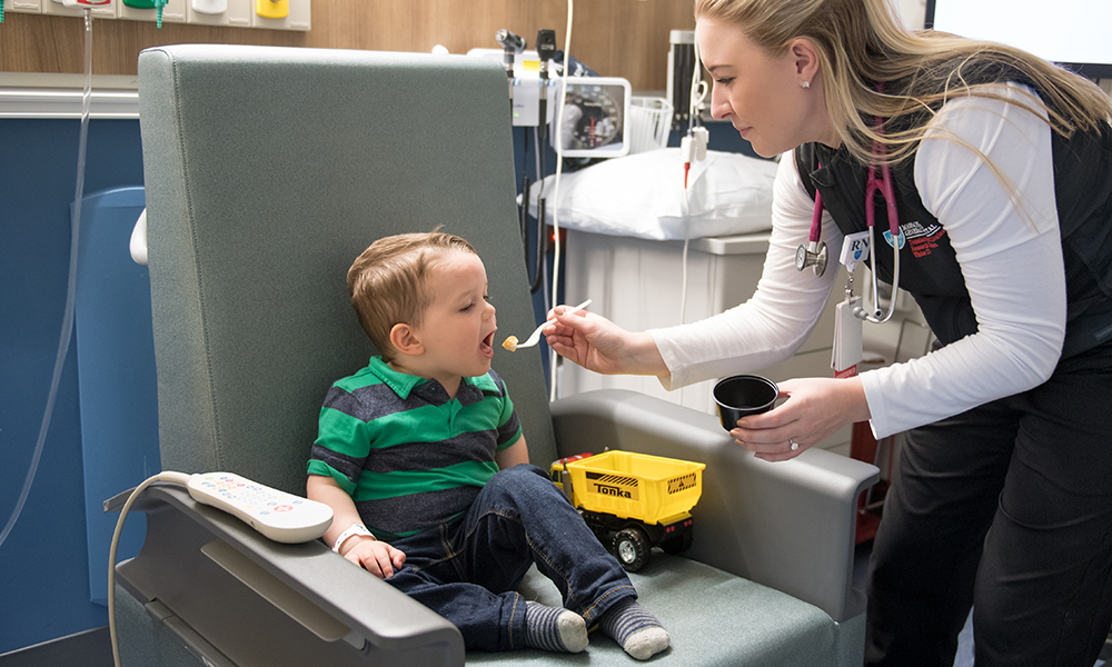 A toddler opens his mouth for a morsel of food, which is offered to him by a staff member. A toddler opens his mouth for a morsel of food, which is offered to him by a staff member.