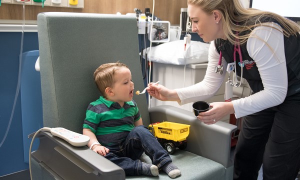 A toddler opens his mouth for a morsel of food, which is offered to him by a staff member. A toddler opens his mouth for a morsel of food, which is offered to him by a staff member.