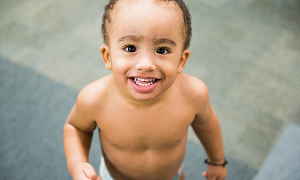 A toddler in a diaper beams up at the camera. A toddler in a diaper beams up at the camera.
