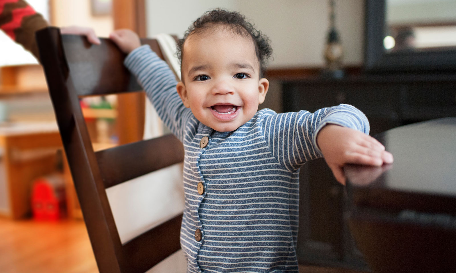A smiling baby stands on a chair. A smiling baby stands on a chair.