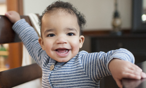 A smiling baby stands on a chair. A smiling baby stands on a chair.