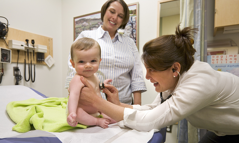 A physician listens to a smiling baby's heart as the mother watches A physician listens to a smiling baby's heart as the mother watches