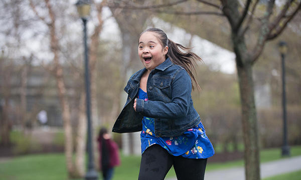 A young girl with Down syndrome runs joyfully through a park. A young girl with Down syndrome runs joyfully through a park.