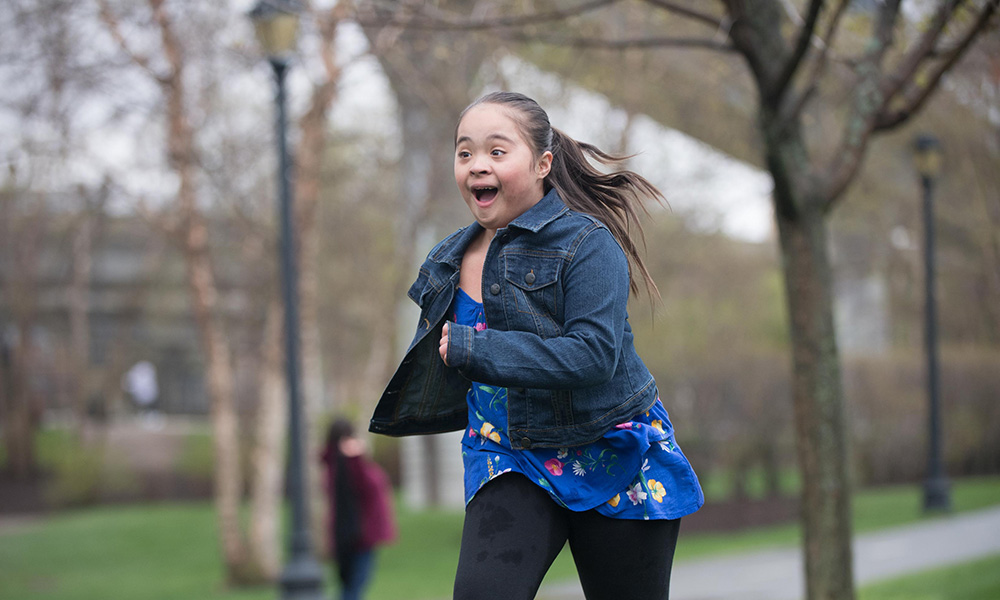 A young girl with Down syndrome runs joyfully through a park. A young girl with Down syndrome runs joyfully through a park.