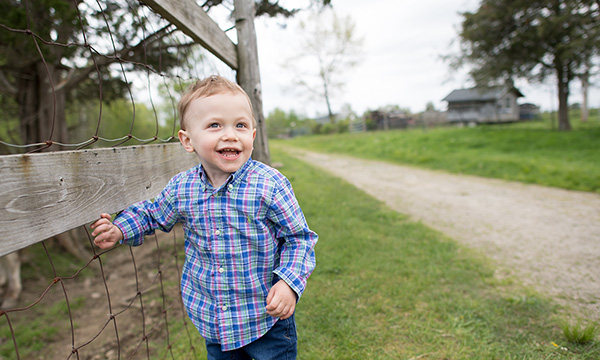 A small boy stands beside a country road, steadying himself on a fence. A small boy stands beside a country road, steadying himself on a fence.