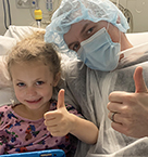 A photo of 6-year-old Alaina Harrington and her father giving a thumbs up to the camera after Alaina's surgery