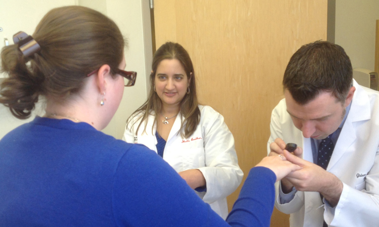 A specialist examines a woman's hand while another specialist looks on. A specialist examines a woman's hand while another specialist looks on.