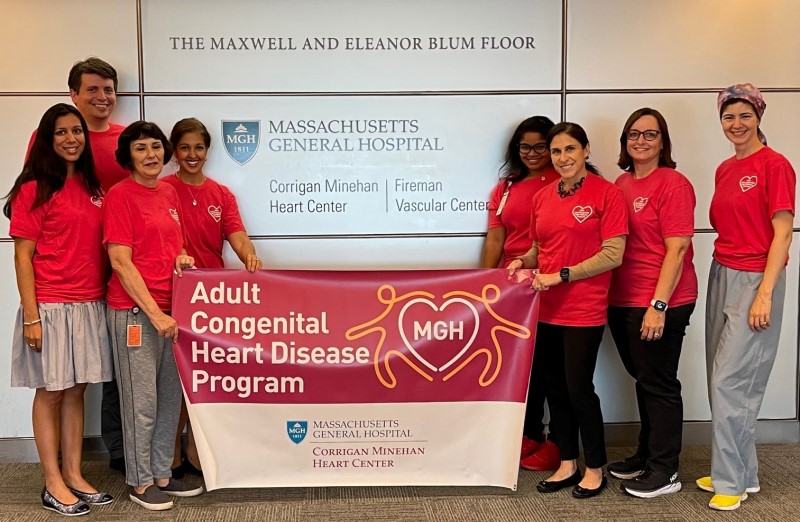 Team members in matching red shirts, holding up a banner for the Adult Congenital Heart Disease Program