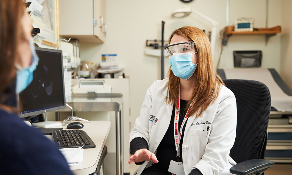 A masked staff person assists a masked patient A masked staff person assists a masked patient