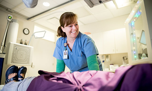 A technologist talks with a patient on an exam table