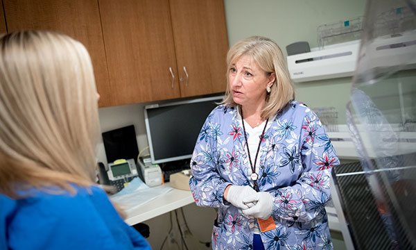 This image was taken in 2019, prior to the hospital's universal mask policy. A breast technologist talks with a patient in an exam room