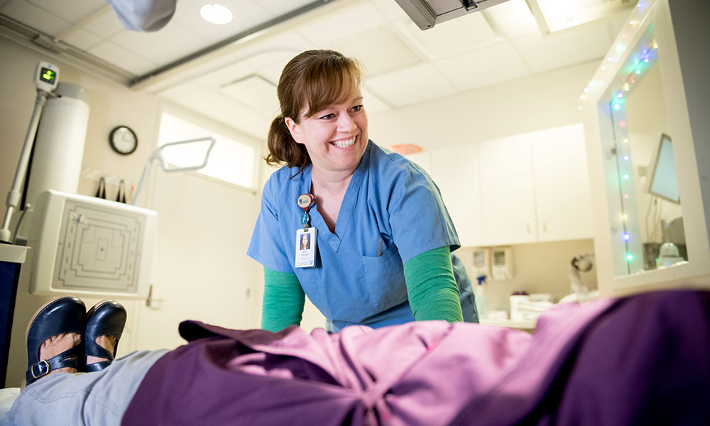 A technologist talks with a patient on an exam table