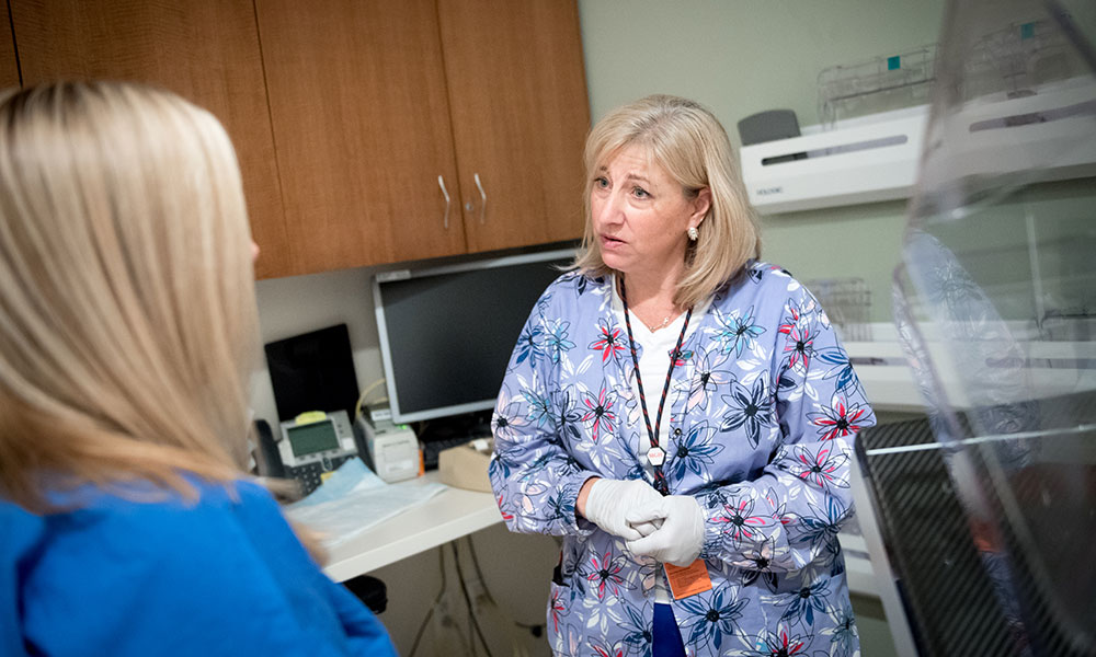 This image was taken in 2019, prior to the hospital's universal mask policy. A breast technologist talks with a patient in an exam room