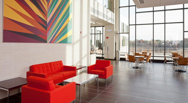 The sunlit lobby, with a cluster of bright red couches under a colorful abstract painting in the foreground. The sunlit lobby, with a cluster of bright red couches under a colorful abstract painting in the foreground.