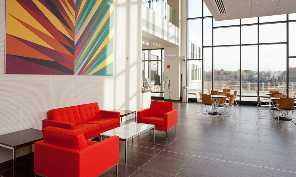 The sunlit lobby, with a cluster of bright red couches under a colorful abstract painting in the foreground. The sunlit lobby, with a cluster of bright red couches under a colorful abstract painting in the foreground.