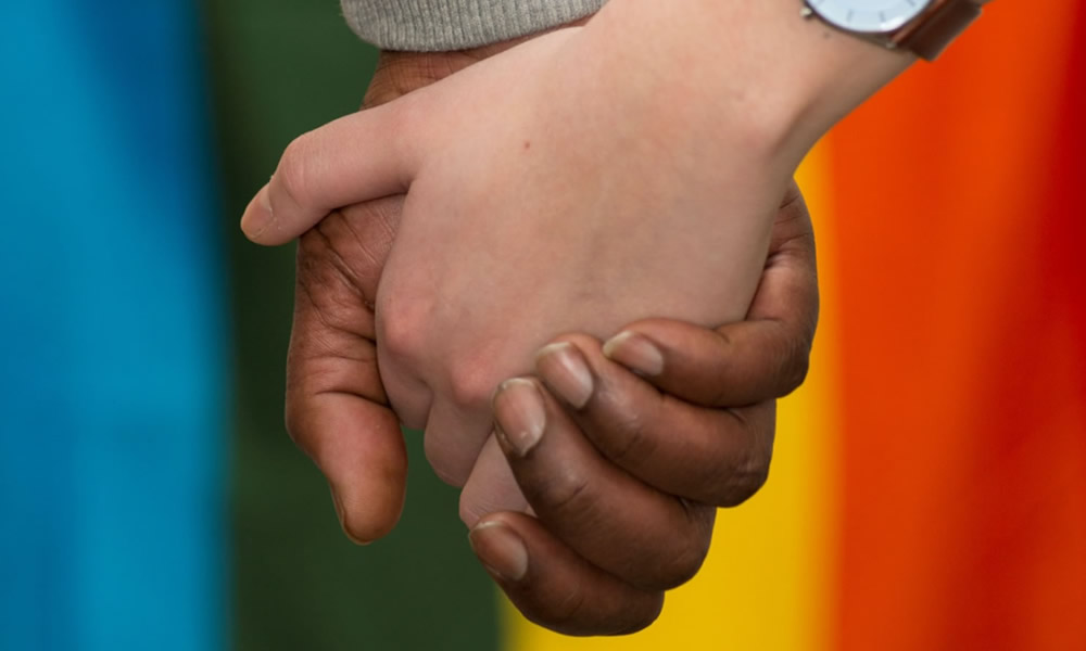 Couple holding hands in front of rainbow flag Couple holding hands in front of rainbow flag