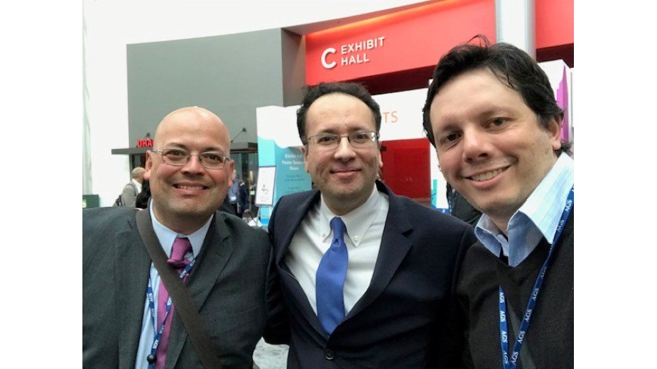Three men stand in a convention hall with the sign for Exhibit Hall C in the background. Three men stand in a convention hall with the sign for Exhibit Hall C in the background.