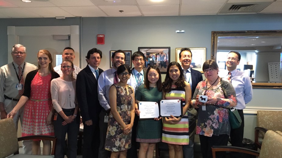 Two young women holding up their diplomas, with the rest of the department posing behind them. Two young women holding up their diplomas, with the rest of the department posing behind them.