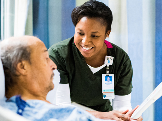 image of a nurse at a patient's bedside reviewing a care plan